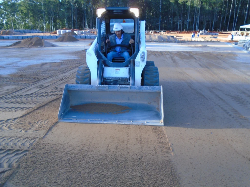 Mini carregadeira Bobcat realizando espalhamento de areia para pavimentação intertravada